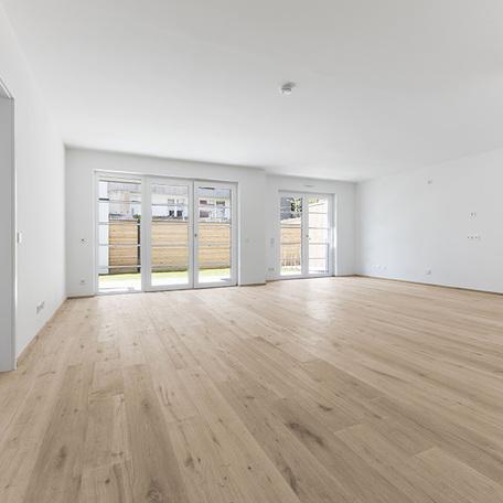 Wohnung von innen mit grossem Wohnzimmer und Fensterfront führt raus auf die Terasse und in den Garten