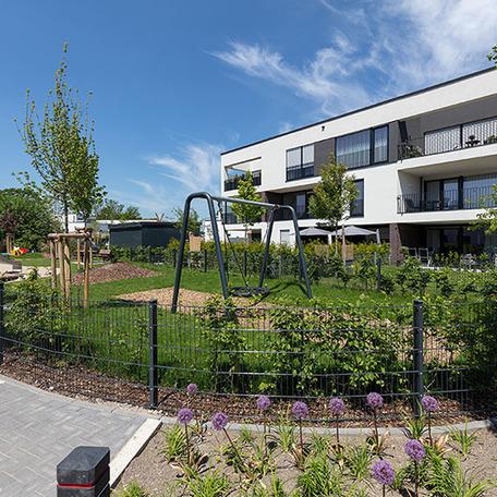 Wohnungen mit weissen Fassaden, Spielplatz, Sandkasten, Schaukel und Kletterhaus
