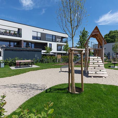 Spielplatz mit Kletterhaus, Rutsche, Sandkasten, Baenken und den Wohnungen im Hintergrund