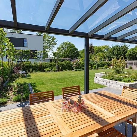 Gartenansicht von der Perspektive der ueberdachten Terasse mit Moebeln und Blumenbeet