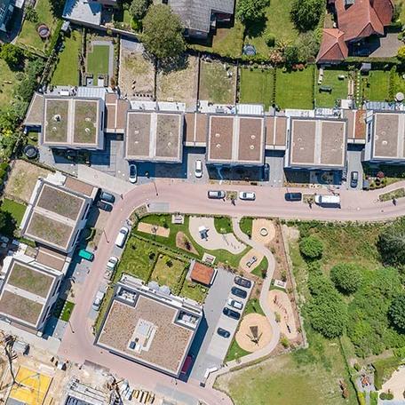 Drohnenansicht der Daecher aller Wohnungsgebaeude mit Auffahrten, Strasse, Gärten und Spielplatz
