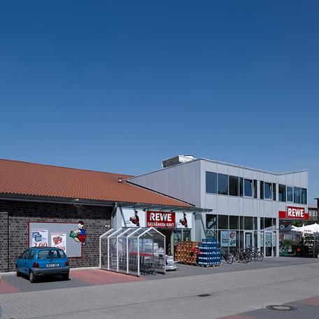 Eingang des Fachmarktzentrum in Recklinghausen von aussen mit grauer Fassade, Rewe Logo, Parkpaetzen und Einkaufswaegen