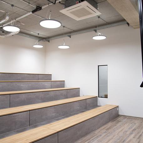 Meetingraum des Gewerbegebaeude Kraemer in Wuppertal mit weissen Waenden und Sitzmoeglichkeiten durch lange Baenke mit Holzsitzflaechen und Betonoptik