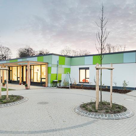 Pflasterung und Pflanzenbeete mit dem gruenen Gebaeude der Kindertagesstaette in Wuppertal im Hintergrund