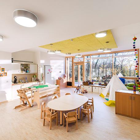 Raum für eine Gruppe von Kindergartenkindern mit vielen Spielzeugen, Moebeln, kleiner Kueche und einer großen Fensterfront die in den Garten fuehrt der Kindertagesstaette in Wuppertal