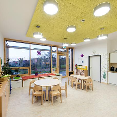 Raum für eine Gruppe von Kindergartenkindern mit vielen Spielzeugen, Moebeln, kleiner Kueche und einer großen Fensterfront die in den Garten fuehrt der Kindertagesstaette in Wuppertal