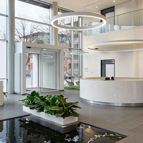 Weisse Empfangstresen und Eingang des Erweiterungsbau eines Reiseveranstalters mit einem Blumenbeet