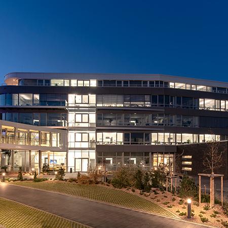 Nachtaufnahme des beleuchteten Erweiterungsbaus eines Reiseveranstalter von aussen mit angelegtem Beet