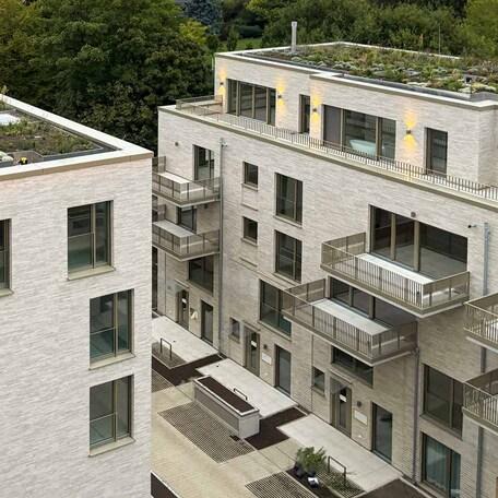Drohnenaufnahme von zwei Wohnhaeusern des Rohbaus in Duesseldorf mit aufwendiger hochwendiger Klinkerfassade, Dachbegruenung, Balkoenen, Terrassen, Eingaengen und Gehwegen