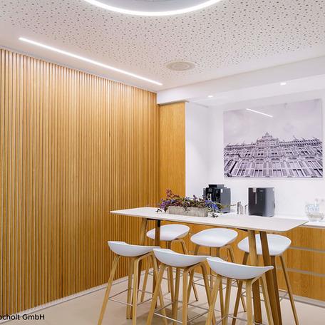 Pausenraum mit Stehtischen, Hockern und zwei Kaffeemaschinen im Hintergrund und einer beleuchteten Holzwand der sanierten Gewerbeflaeche in Bocholt