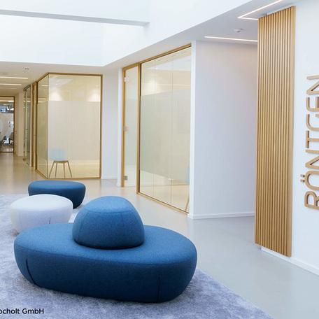 Flur mit weissen Waenden, Glastrenner mit Milchglasfolien und Tueren als Eingang zu Praxisraeumen und mit Fokus auf kleine blaue Sofa auf einem Teppich
