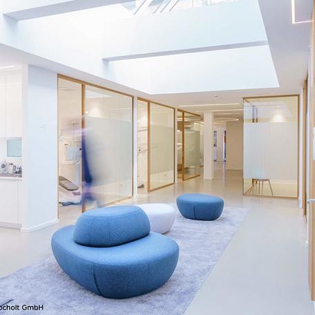 Flur mit weissen Waenden, Glastrenner mit Milchglasfolien und Tueren als Eingang zu Praxisraeumen und mit Fokus auf kleine blaue Sofa auf einem Teppich