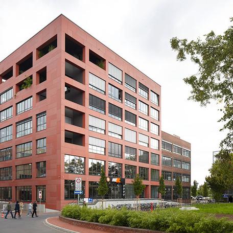 Gebaeude der umgebauten Schwanenhoefe in Duesseldorf mit Zufahrt, vielen Fenstern, roter Fassade und Fahrradstaendern