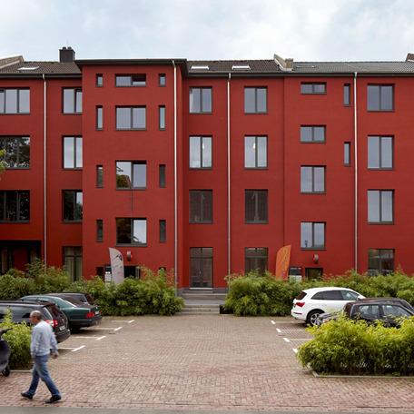 Teil des Gebaeudes der umgebauten Schwanenhoefe in Duesseldorf mit roter Fassade und einem Parkplatz
