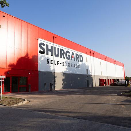 Selbstlagerhalle Shurgard in Neuss von aussen mit grossem Logo an der rot weissen grauen Fassade und einem Eingang