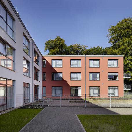 Seniorenpflegezentrum in Alsdorf von aussen mit Terasse, braun-roter und weisser Fassade, Gehwegen und angelegten Beeten