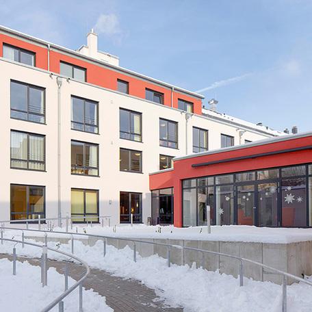Innenhof des Seniorenpflegezentrum in Haan von aussen mit beige bis roetlichen Fassaden, grossen Fenstern und Gehweg