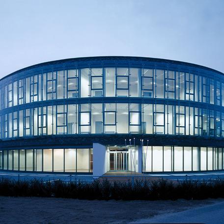 Verwaltungsgebaeude in Bocholt von aussen mit gewolbter beleuchteter Glasfront am Abend