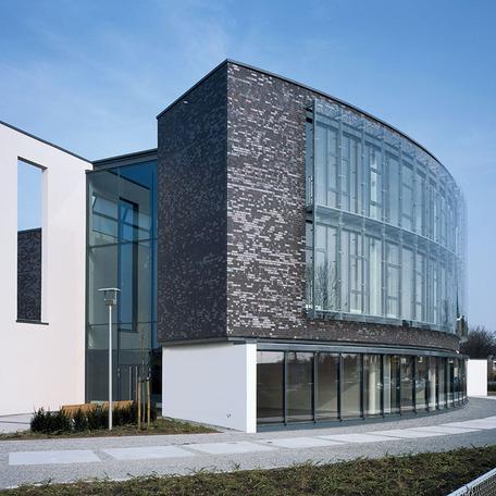 Verwaltungsgebaeude in Bocholt von aussen mit Fokus auf das Ende der gewolbten Glasfront mit grauer Fassade am Tag