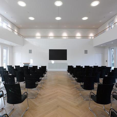 Versammlungsraum des Verwaltungsgebaeude in Duisburg mit Holzboden, schwarzen Stuehlen, Rednerpult, Fernseher und weissen Waenden