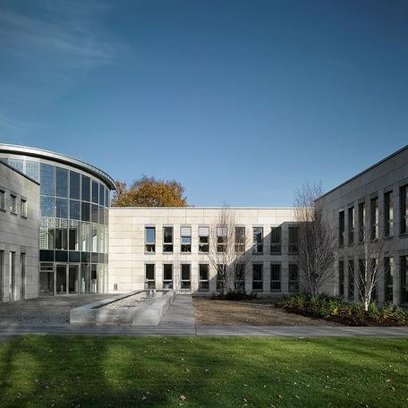 Eingang des Verwaltungsgebaeude in Duisburg von aussen mit gewoelbter Glasfront, beiger Fassade, Fussweg und angelegte Pflanzenbeete