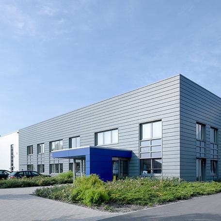 Verwaltungsgebaeude und Produktionshalle in Duisburg von aussen mit Eingang, grauer Fassade und Parkplaetzen
