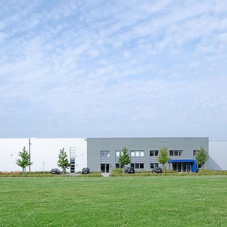 Frontalansicht des Verwaltungsgebaeude und Produktionshalle in Duisburg von aussen mit grauer Fassade, Parkplaetzen und Wiese