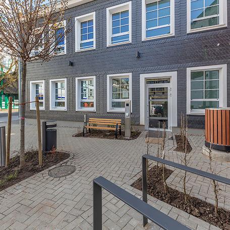 Fokus auf den Eingang des Gebaeude der Stadtsparkasse nach dem Wiederaufbau in Schwelm von aussen mit grauer Fassade, vielen Fenstern, Pflanzenbeete und einer Sitzbank