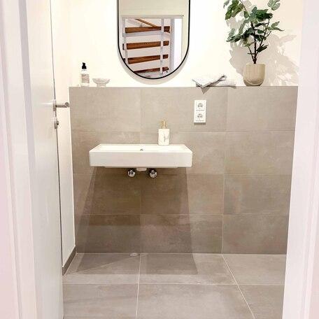 Bad einer Musterwohnung des Bauprojektes Duesseldorf Oberbilk mit Waschbecken, Spiegel, weisser Tapete und braungrauen Fliesen