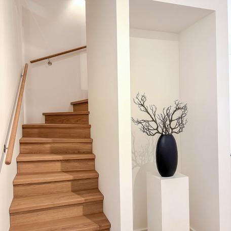 Flur einer Musterwohnung des Bauprojektes Duesseldorf Oberbilk mit Treppe aus Holz welche in die zweite Etage fuehrt, Deko und weisser Tapete