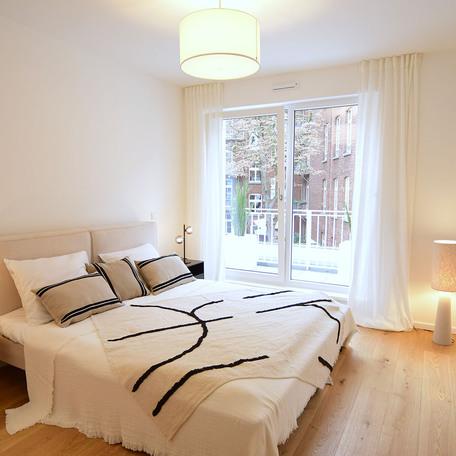 Schlafzimmer einer Musterwohnung des Bauprojektes Duesseldorf Oberbilk mit Bett, Holzboden und Blick aus dem Fenster