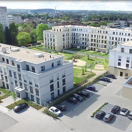 Drohnenansicht des Wohn- und Gewerbekomplexes in Bonn von aussen mit beiger Fassade, Garten, Terrassen, Spielplatz, Wiese und Parkplaetzen