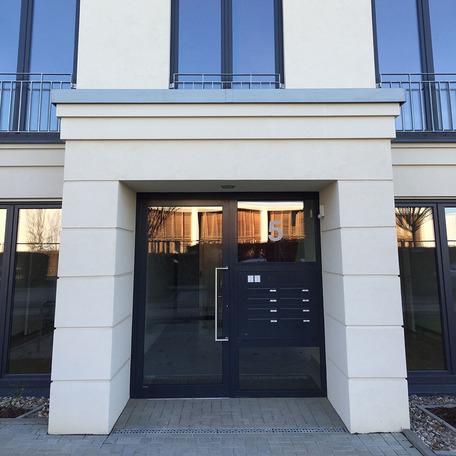 Eingang des Wohn- und Gewerbekomplexes in Bonn von aussen mit beiger Fassade und schwarzen Tuer- und Fensterrahmen