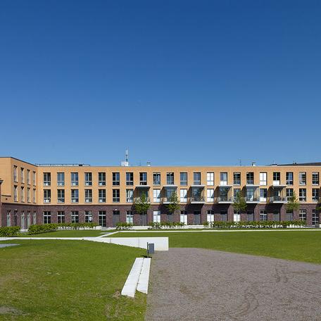 Wohn- und Gewerbekomplex in Duesseldorf von aussen mit Fokus auf die grosse gruene Wiese Schotterweg und die Gehwege