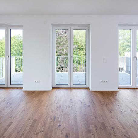 Wohnzimmer einer Wohnung in Bocholt am Fluss mit großen Glastueren als Ausgang auf den grossen Balkon und weissen Waenden