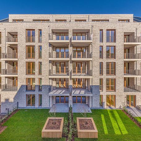 Ein Gebaeude des Wohnkomplexes Moll in Duesseldorf im Fokus mit beiger Klinkerfassade, Balkonen, Terrassen und Gaerten