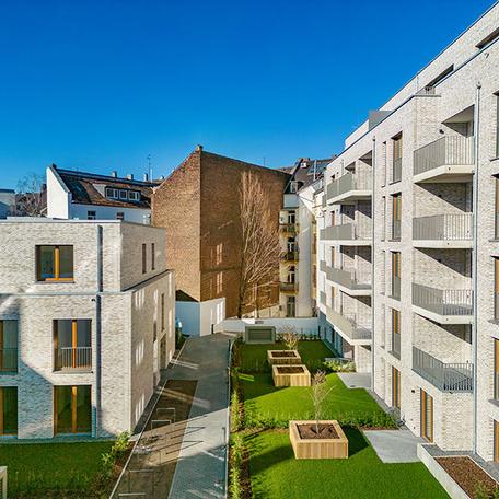 Seitenansicht zwischen den beiden beigen Gebaeuden des Wohnkomplexes Moll in Duesseldorf mit Balkonen, Gaerten und Gehwegen