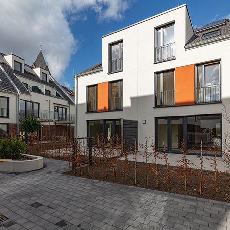 Haeuserreihe des Wohnquatiers in Angermund von aussen mit beiger Fassade und orangen Akzenten, Terassen, Gaerten, Balkonen und Gehwegen