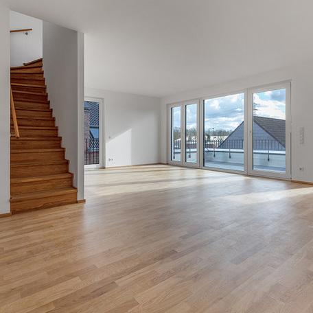 Wohnzimmer einer Wohnung des Wohnquatiers in Angermund mit weissen Waenden, Holzboden, grosser Fensterfront mit Tuer, Balkon und Treppe
