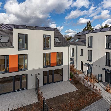Haeuserreihe des Wohnquatiers in Angermund von aussen mit beiger Fassade und orangen Akzenten, Terassen, Gaerten, Eingaengen und Gehwegen