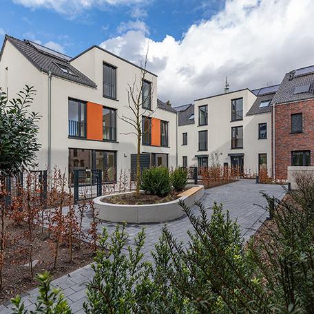 Haeuserreihe des Wohnquatiers in Angermund von aussen mit beiger Fassade und orangen Akzenten, Terassen, Gaerten, Eingaengen, angelegten Beeten und Gehwegen
