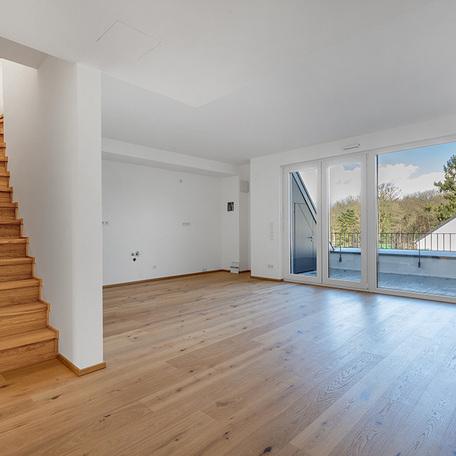 Wohnzimmer einer Wohnung des Wohnquatiers in Angermund mit weissen Waenden, Holzboden, grosser Fensterfront mit Tuer, Balkon und Treppe