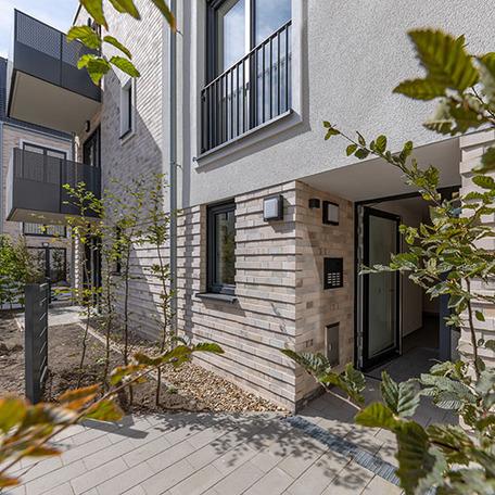 Eingang eines Wohngebaeudes in Krefeld mit beiger Fassade, Fenstern, Balkonen, Gehweg und Beeten