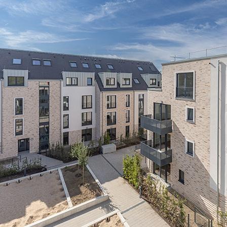 Aussicht der Dachterrasse auf die Wohngebaeude in Krefeld im Innenhof mit beiger Fassade, grauem Dach, Fenstern, Balkonen und Gehwegen mit Eingaengen