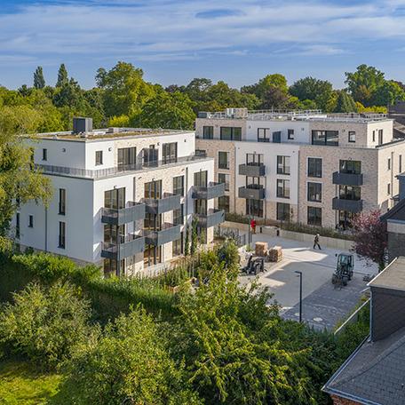 Drohnenansicht des Hinterhofs mit zwei Wohngebaeuden im Fokus mit beiger Fassade, Balkonen, Fenstern, Gaerten, Gehwegen und Parkplatz