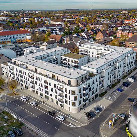 Drohnenansicht des gesamten Wohnquatiers in Moers mit weisser Fassade, Balkonen, Terrassen, Parkplaetzen und Strassenanbindung