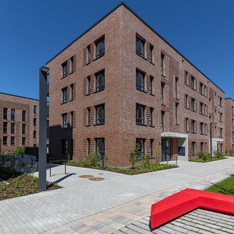 Eine Haeuserreihe im Fokus des Wohnquatiers in Muenster mit brauner Klinkerfassade, Eingaengen, Gehwegen und roter Sitzmoeglichkeit