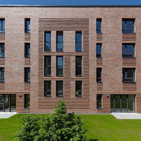 Frontalansicht auf eine Haeuserreihe des Wohnquatiers in Muenster mit brauner Klinkerfassade, Terrasse und gruener Wiese