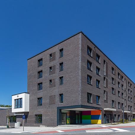 Eingang einer Haeuserreihe des Wohnquatiers in Muenster mit dunkler Klinkerfassade, einer bunt gestrichenen Wand und Strassenanbindung