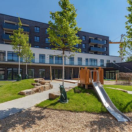 Haeuserreihe des Wohnquatiers in Muenster mit einem Mix aus dunkler Klinkerfassade und beiger Fassade und den Fokus auf die Rutsche des direkt anliegenden Spielplatzes